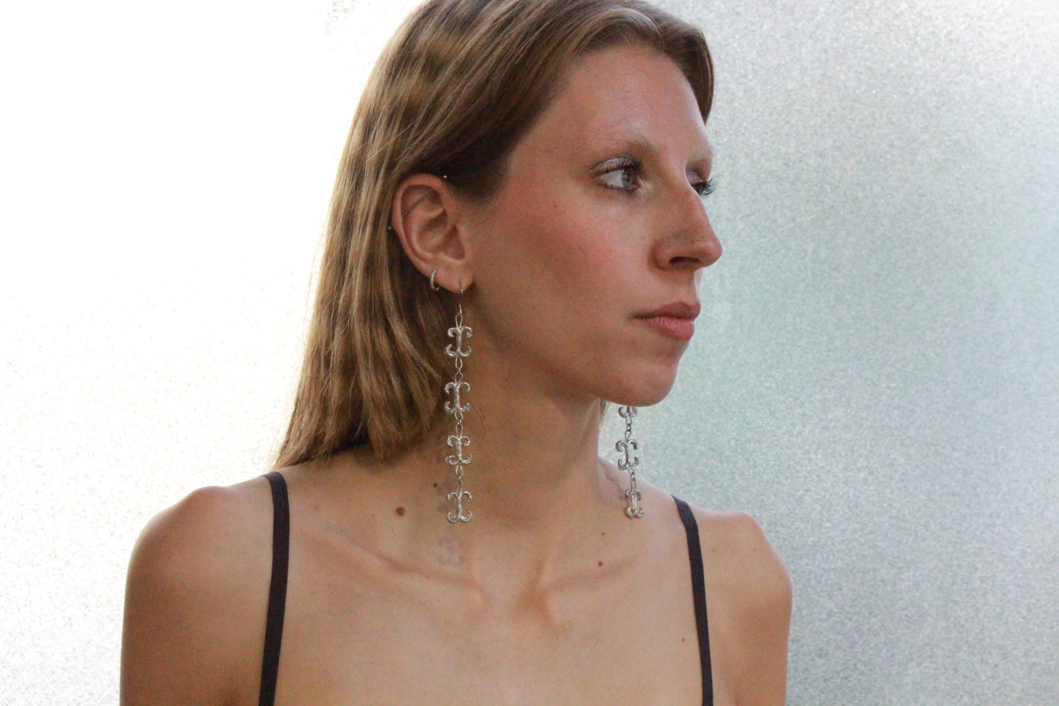 shooting éditorial boucles d'oreilles volutes inspirées de la ferronnerie d'art avec pendentifs fondus individuellement selon un procédé artisanal unique mis au point par la marque de bijoux Lolie, finition argenté