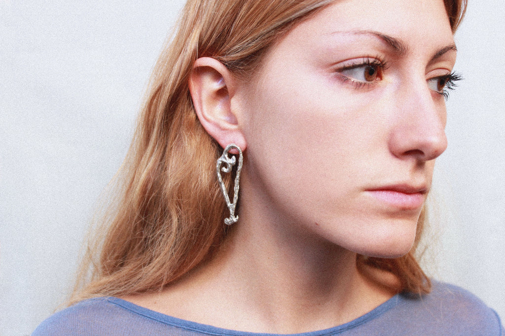close up boucles d'oreilles coeur asymétrique en étain argenté fondu individuellement à la commande selon un procédé artisanal unique mis en place par la marque de bijoux Lolie