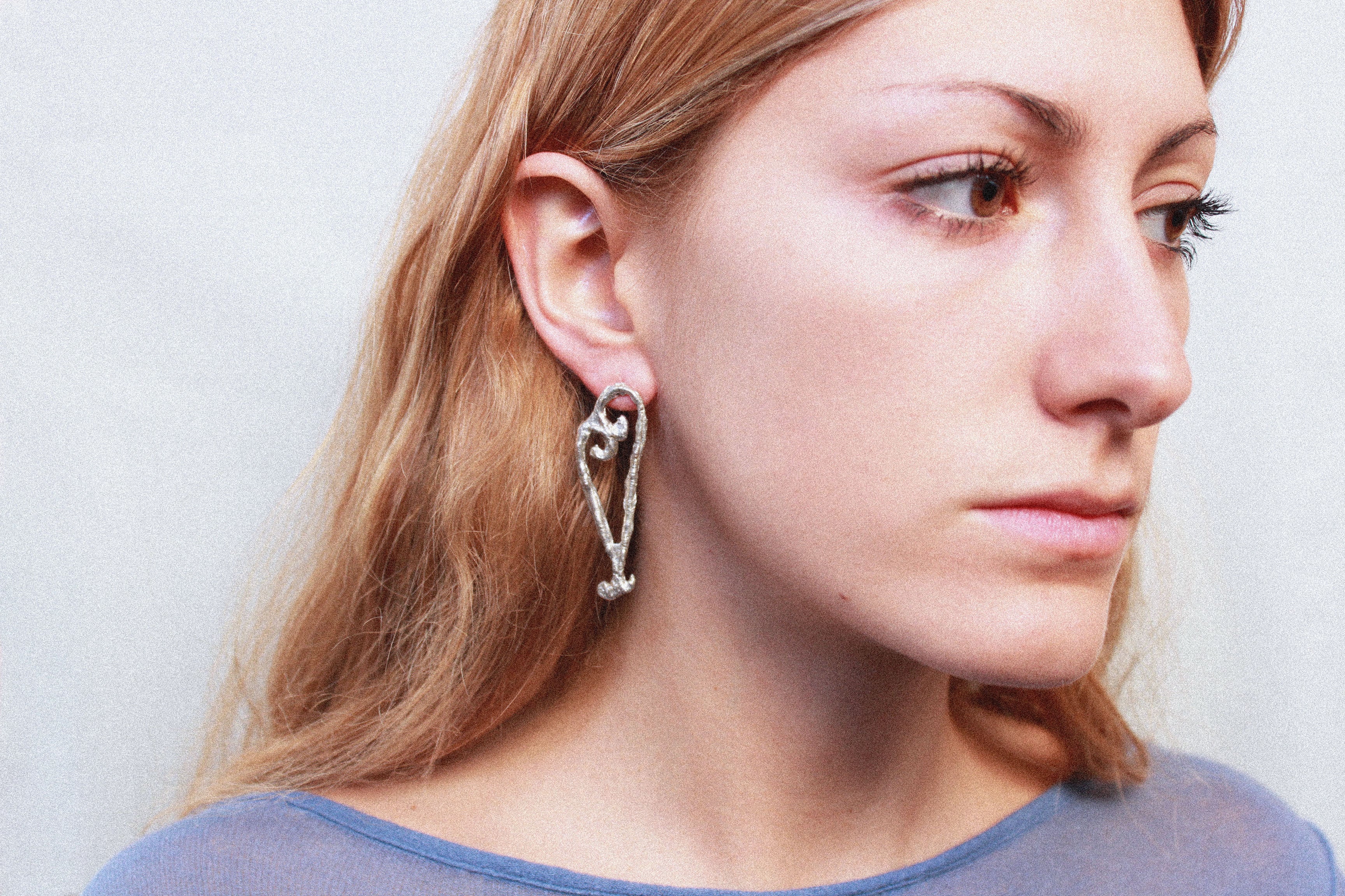 close up boucles d'oreilles coeur asymétrique en étain argenté fondu individuellement à la commande selon un procédé artisanal unique mis en place par la marque de bijoux Lolie