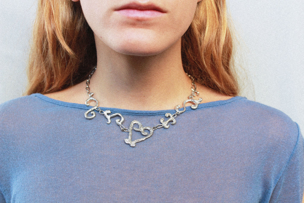 Close up collier inspiré de la ferronnerie d'art avec pendentifs asymétriques fondus individuellement selon un procédé artisanal unique mis au point par la marque de bijoux Lolie, finition argenté, tissu organza lavande