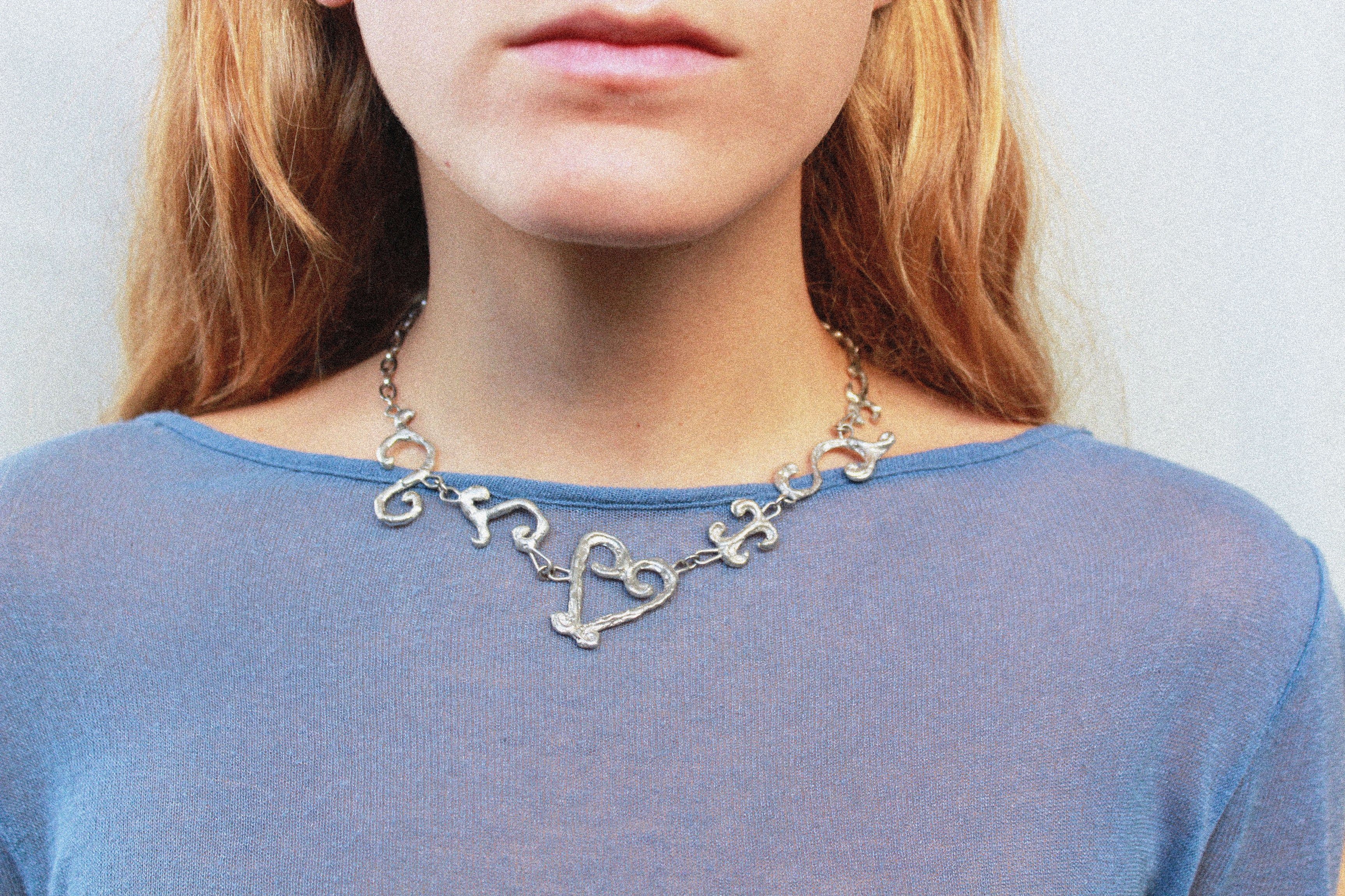 Close up collier inspiré de la ferronnerie d'art avec pendentifs asymétriques fondus individuellement selon un procédé artisanal unique mis au point par la marque de bijoux Lolie, finition argenté, tissu organza lavande