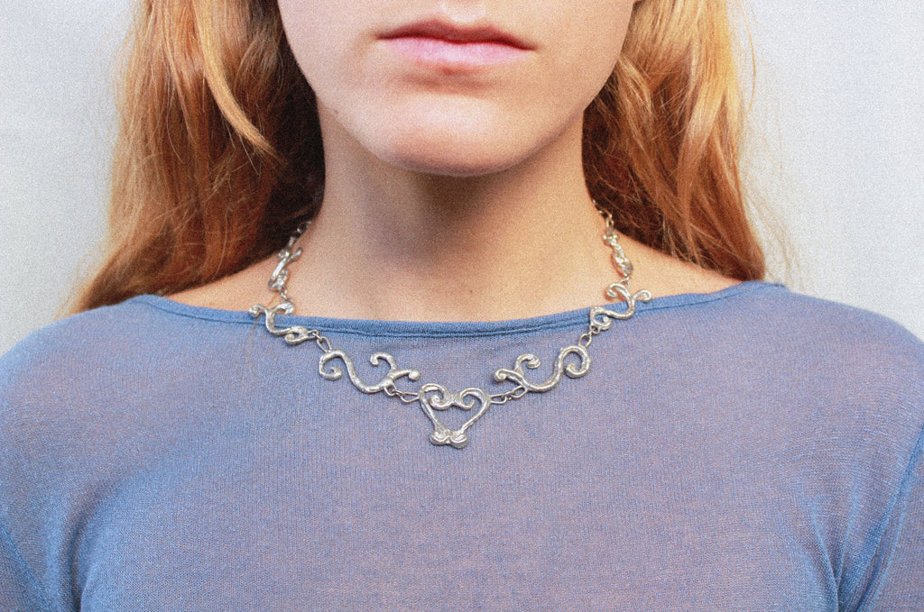 Close up collier inspiré de la ferronnerie d'art avec pendentifs symétriques fondus individuellement selon un procédé artisanal unique mis au point par la marque de bijoux Lolie, finition argenté, tissu organza lavande