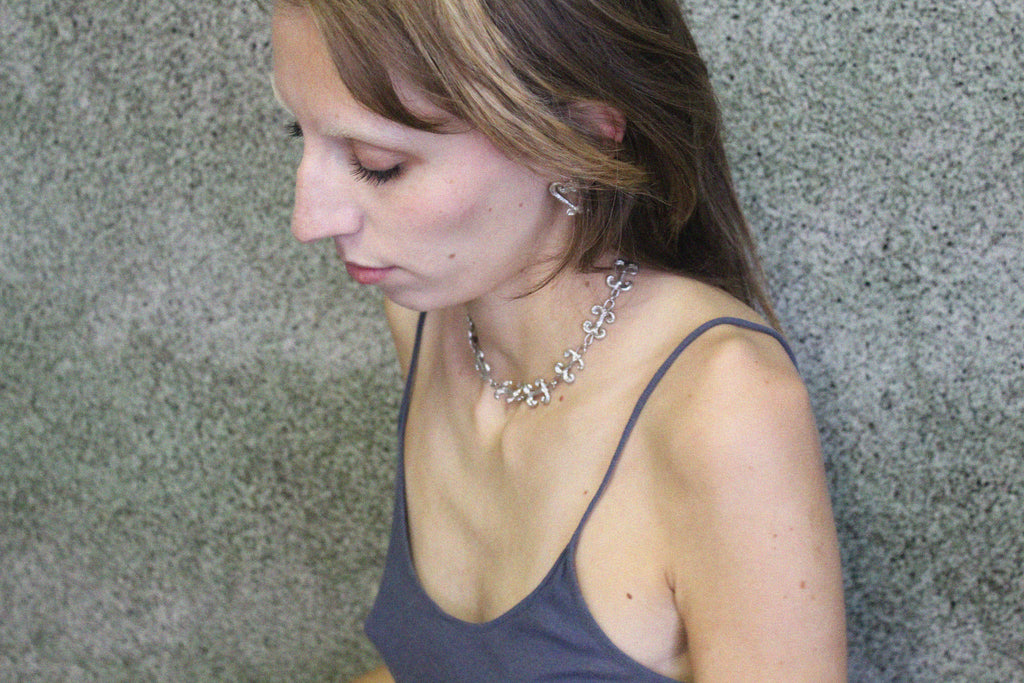 shooting éditorial collier inspiré de la ferronnerie d'art avec pendentifs "volute" fondus individuellement selon un procédé artisanal unique mis au point par la marque de bijoux Lolie, finition argenté, tissu organza lavande