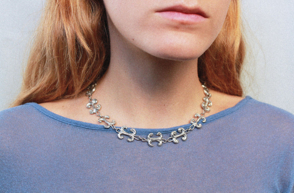 Close up collier inspiré de la ferronnerie d'art avec pendentifs "volute" fondus individuellement selon un procédé artisanal unique mis au point par la marque de bijoux Lolie, finition argenté, tissu organza lavande
