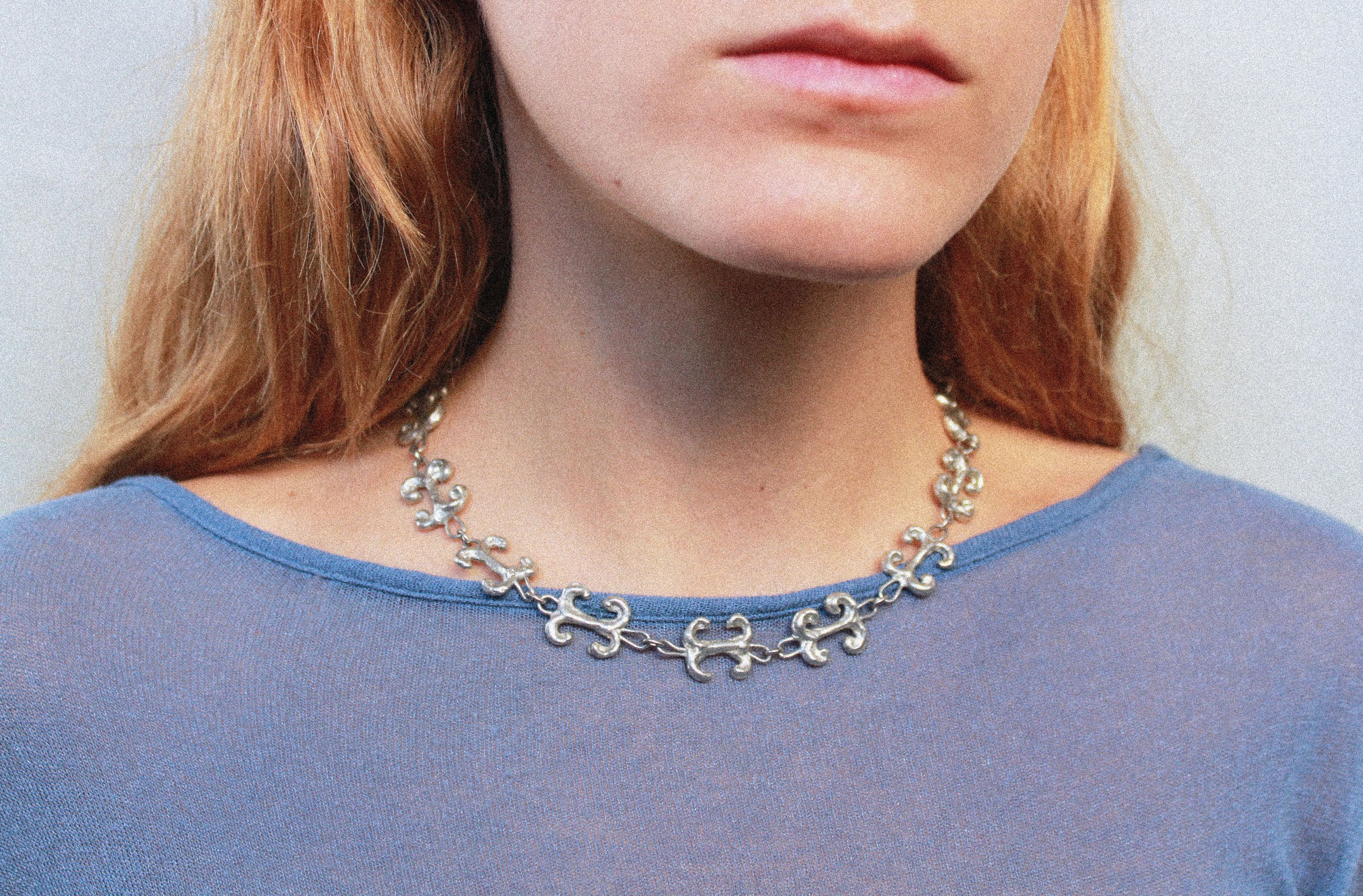 Close up collier inspiré de la ferronnerie d'art avec pendentifs "volute" fondus individuellement selon un procédé artisanal unique mis au point par la marque de bijoux Lolie, finition argenté, tissu organza lavande