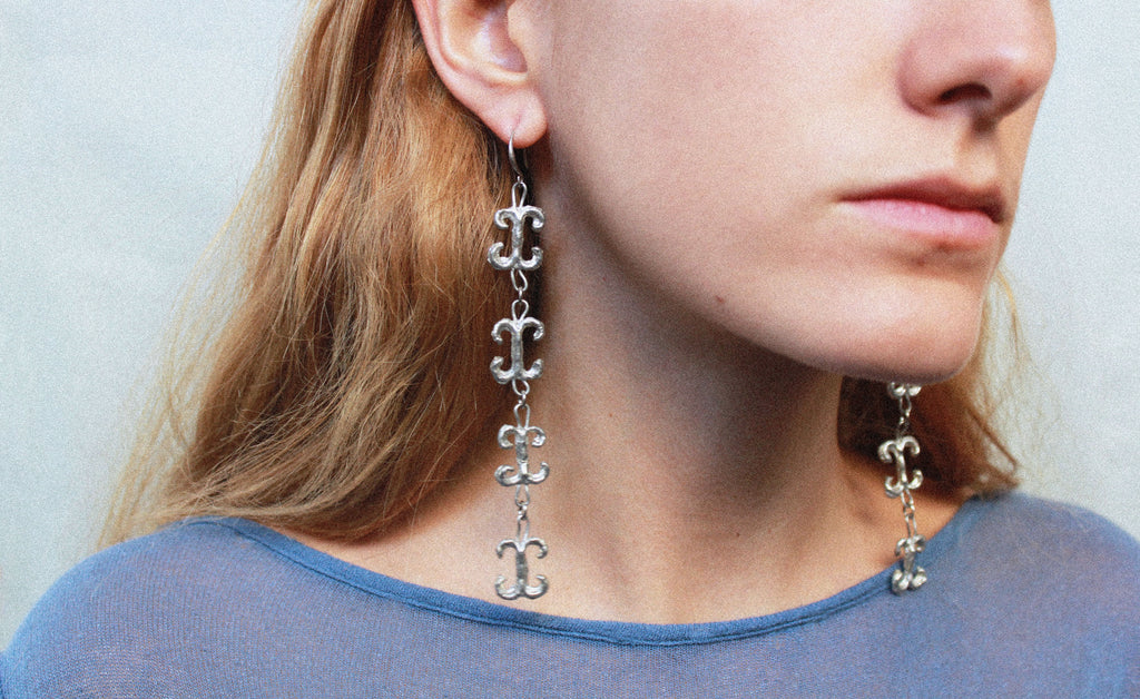 Close up boucles d'oreilles volutes inspirées de la ferronnerie d'art avec pendentifs fondus individuellement selon un procédé artisanal unique mis au point par la marque de bijoux Lolie, finition argenté