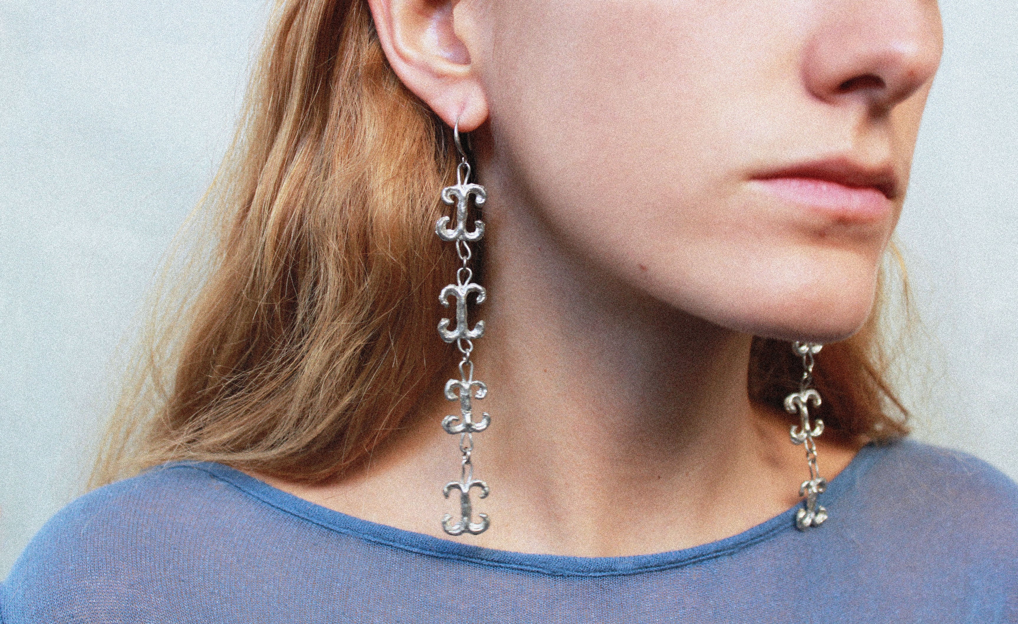 Close up boucles d'oreilles volutes inspirées de la ferronnerie d'art avec pendentifs fondus individuellement selon un procédé artisanal unique mis au point par la marque de bijoux Lolie, finition argenté